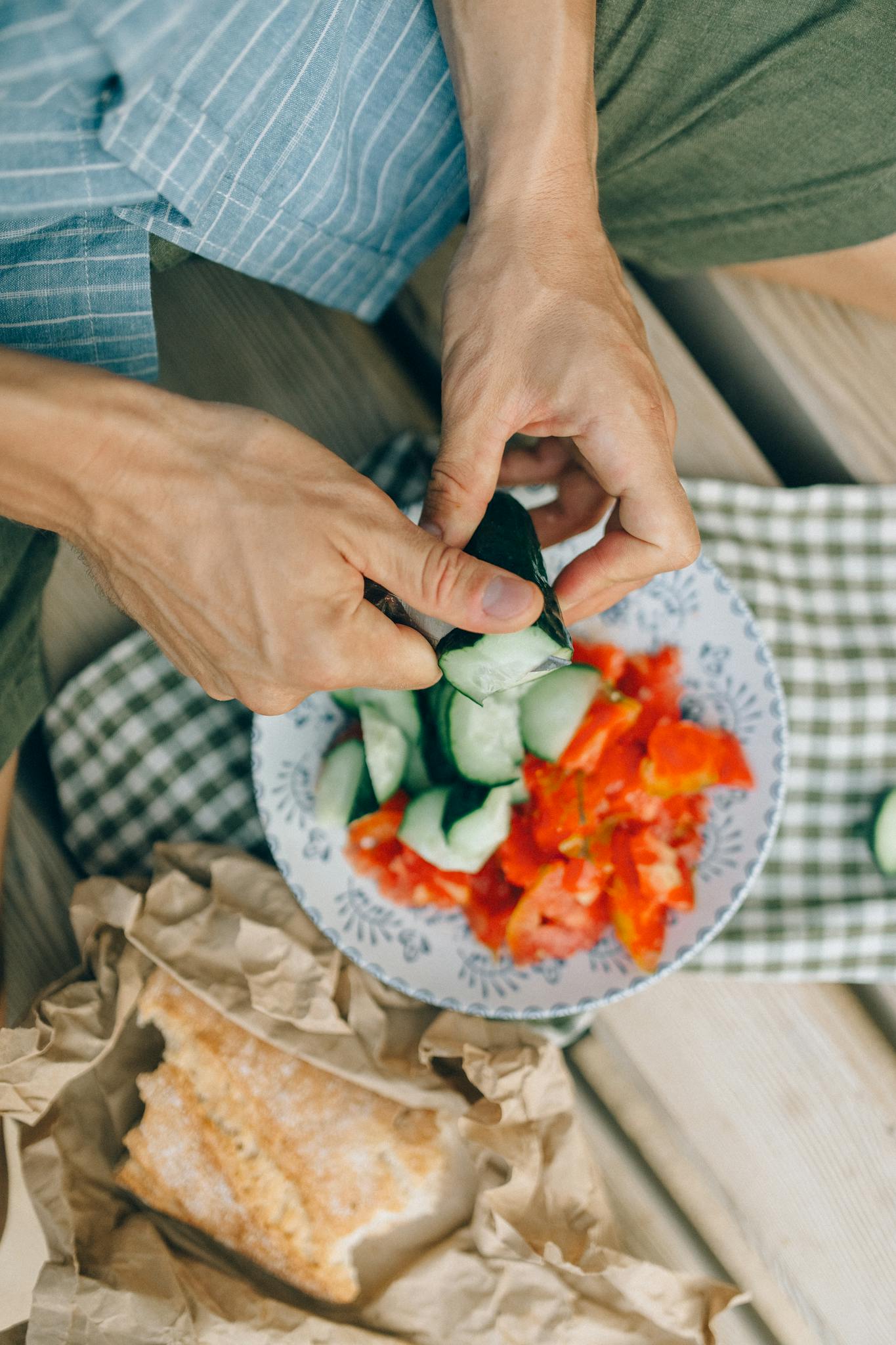 Close-up of hands slicing cucumbers and tomatoes for a healthy salad, indoors.